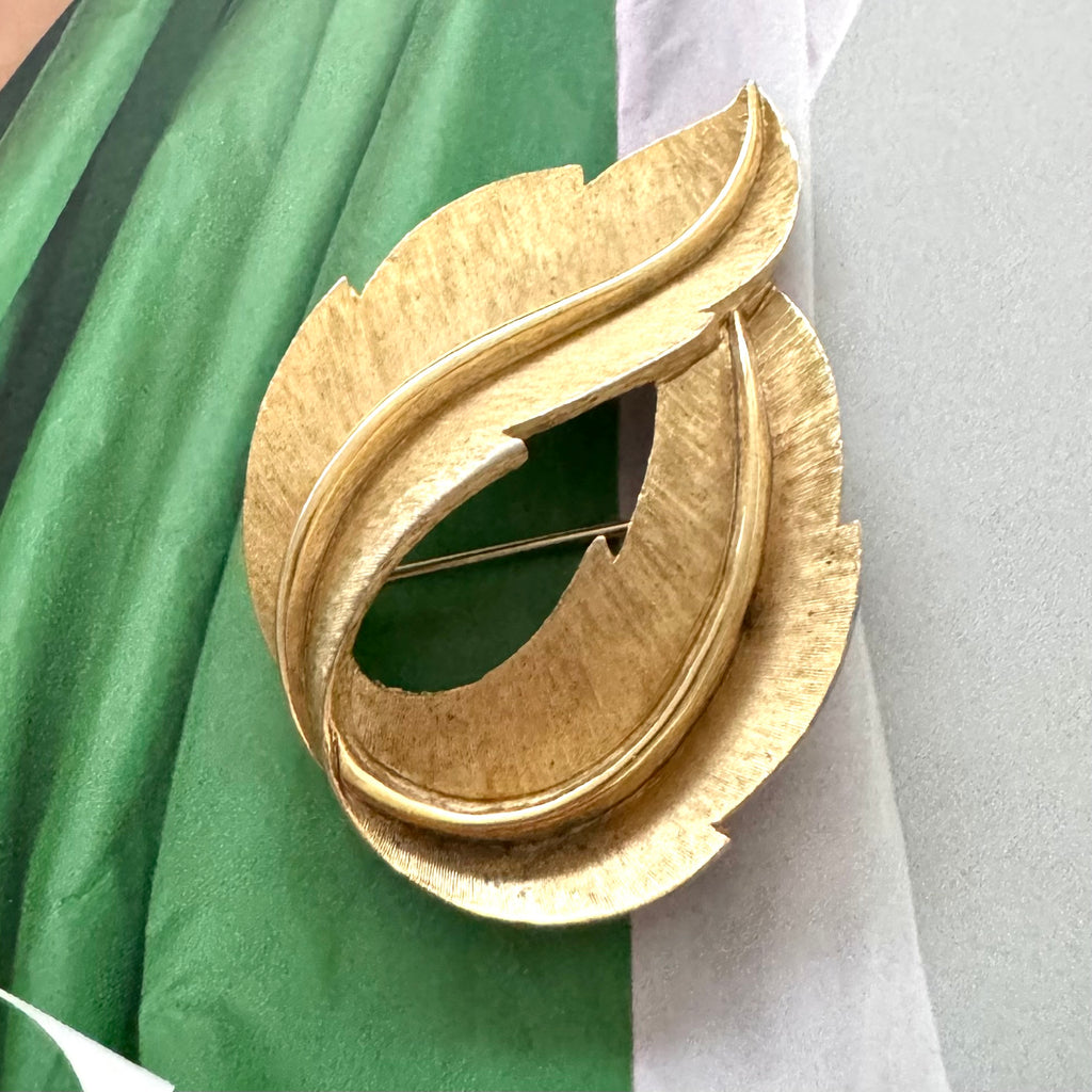 Crown Trifari Gold leaf-shaped brooch on a green and white fabric background