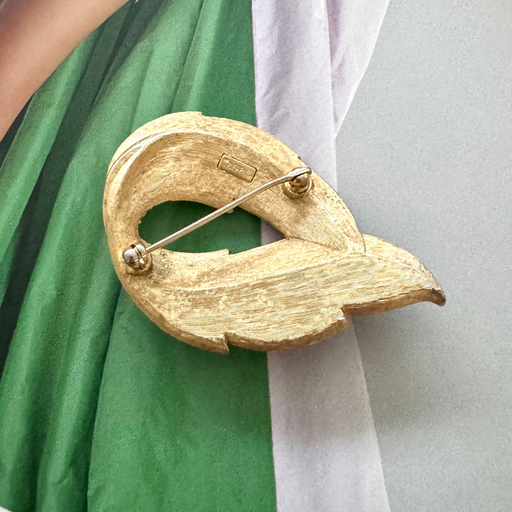Crown Trifari Gold leaf-shaped brooch on a green and white fabric background