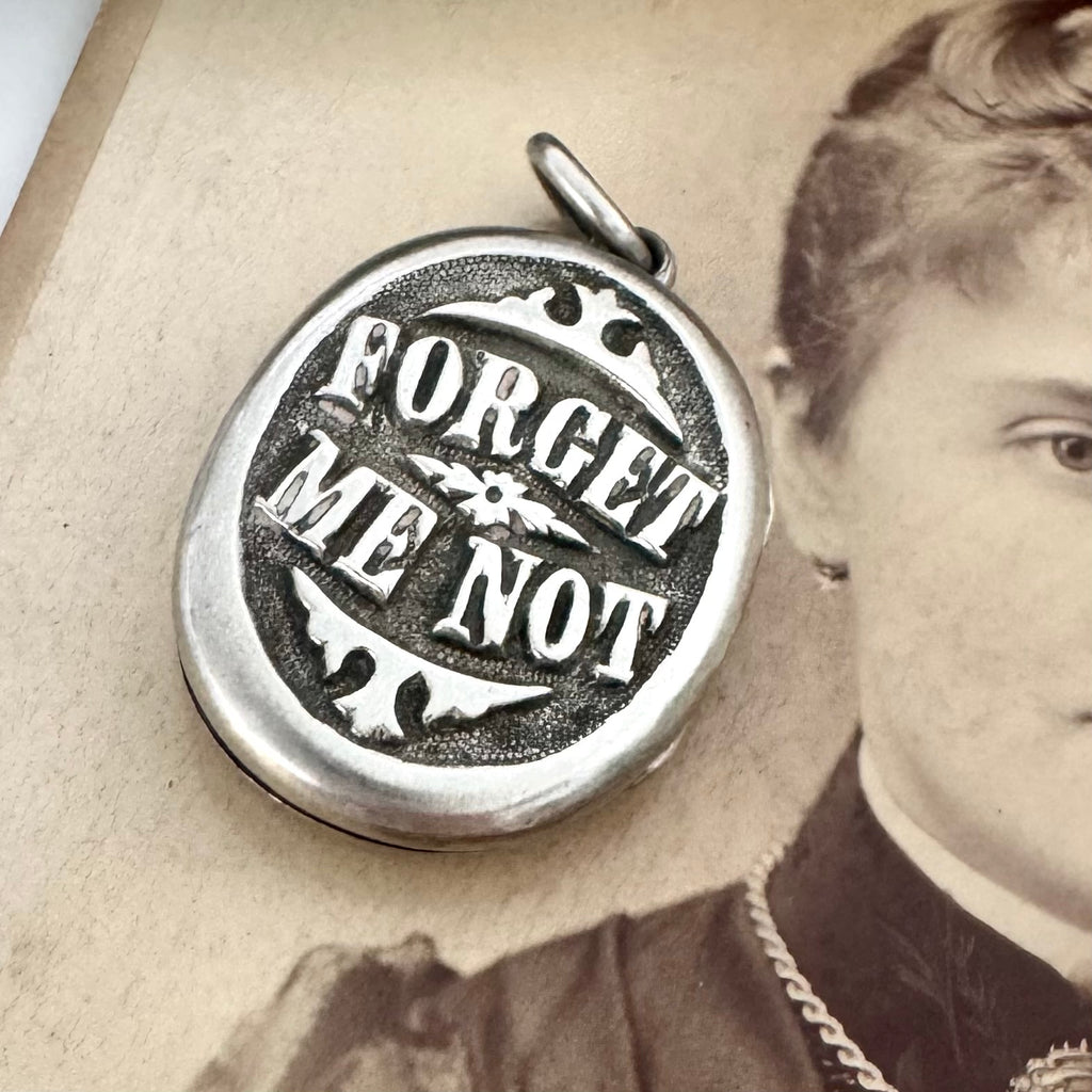 Close up of a Victorian silver plated Forget Me Not locket on a Victorian photograph of a woman wearing a brooch and a locket.