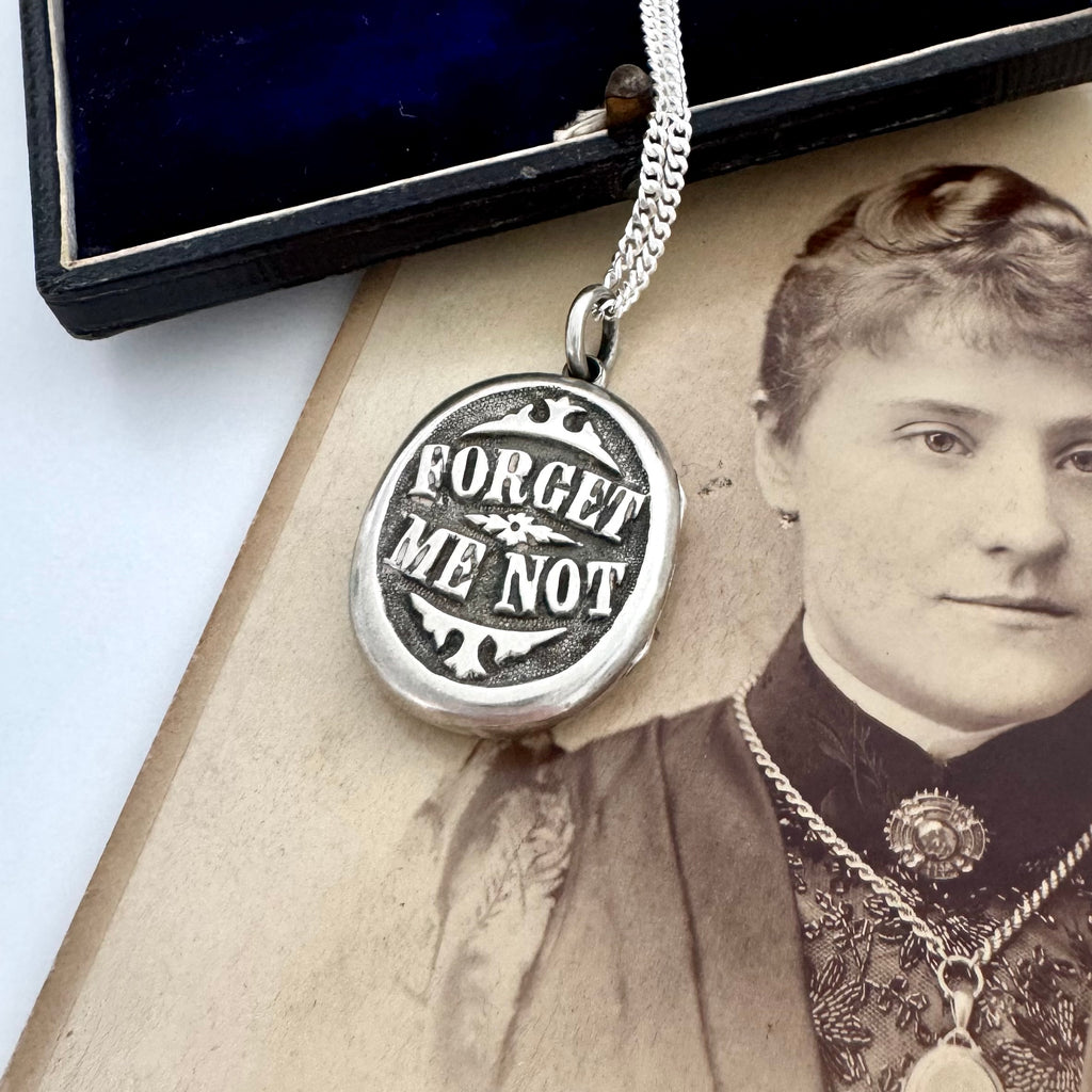 Victorian silver plated Forget Me Not locket on a Victorian photograph of a woman wearing a brooch and a locket. The locket is on a silver chain and is resting on a vintage jewellery box.