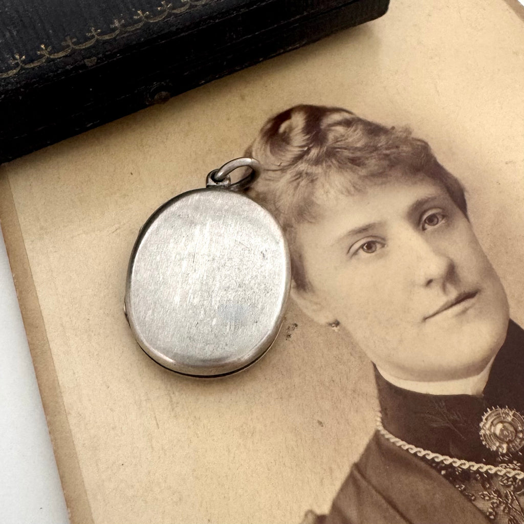 Back of Victorian silver plated Forget Me Not locket on a Victorian photograph of a woman wearing a brooch and a locket.