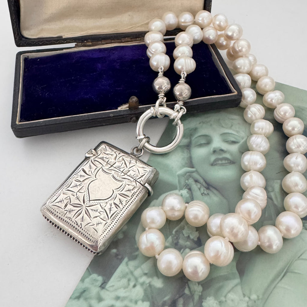 Vonk Jewellery antique sterling silver vesta case on a pearl necklace. The necklace is on a vintage green French postcard and a vintage jewellery box.