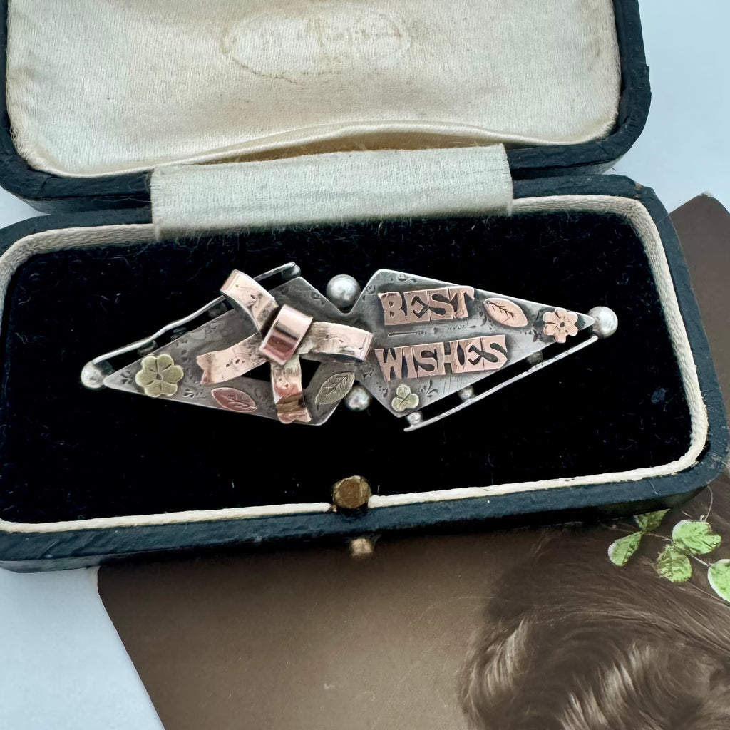 Victorian 1900 antique sterling silver and rose gold sweetheart brooch with the words 'BEST WISHES' in raised lettering, styled on a vintage jewellery box