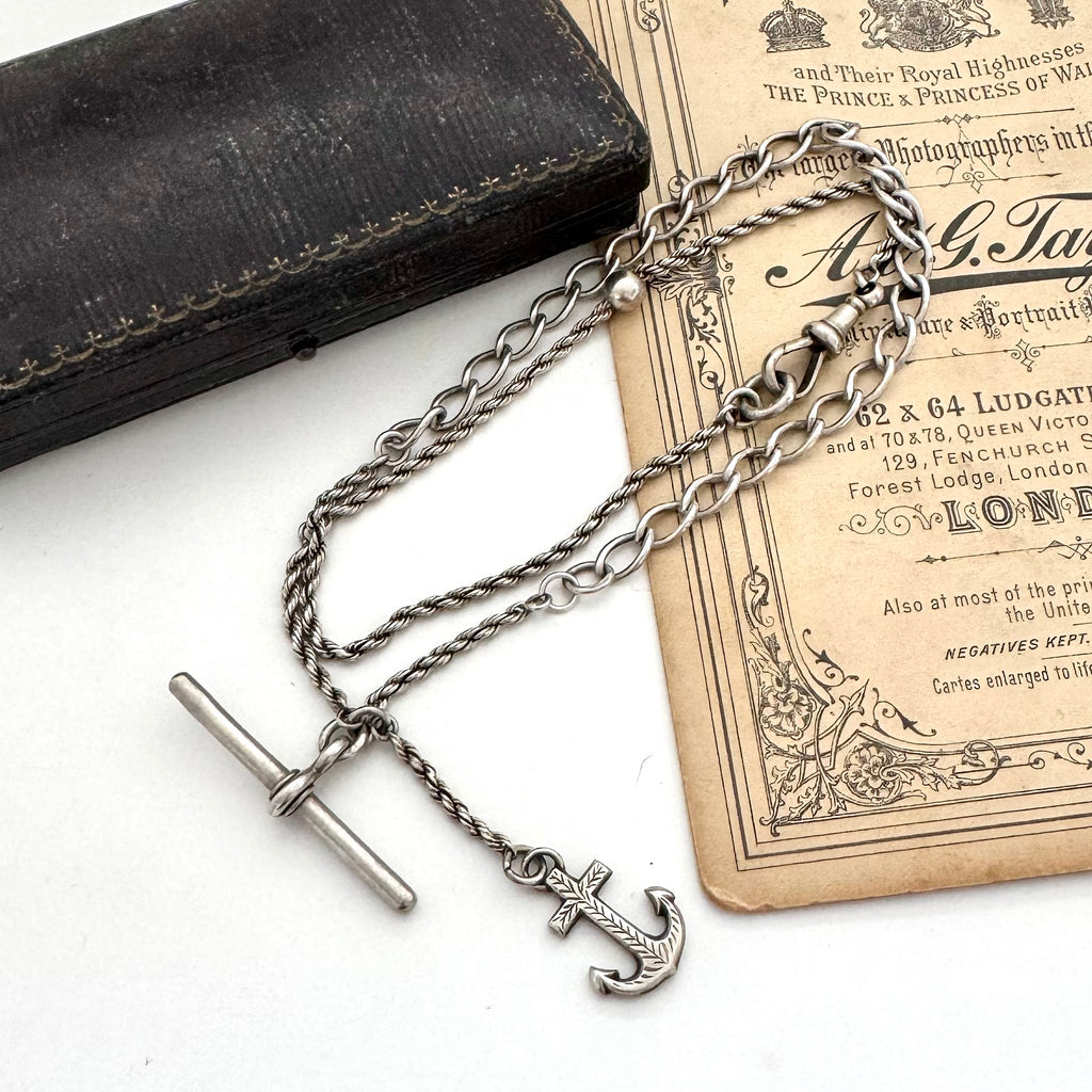 Antique silver albertina chain necklace with an anchor pendant on a vintage box and antique advertising material.
