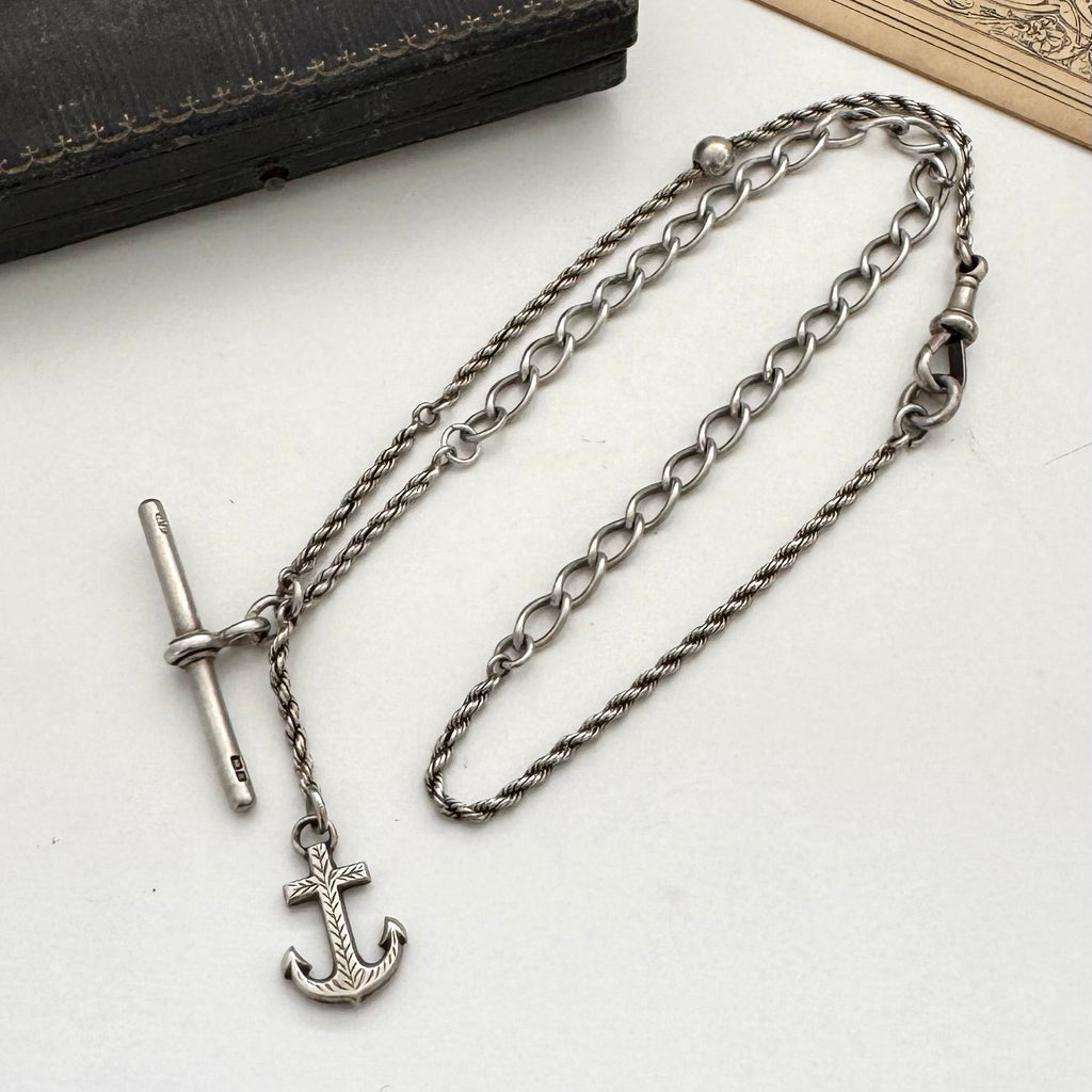 Antique silver albertina chain necklace with an anchor pendant on a vintage box and antique advertising material.