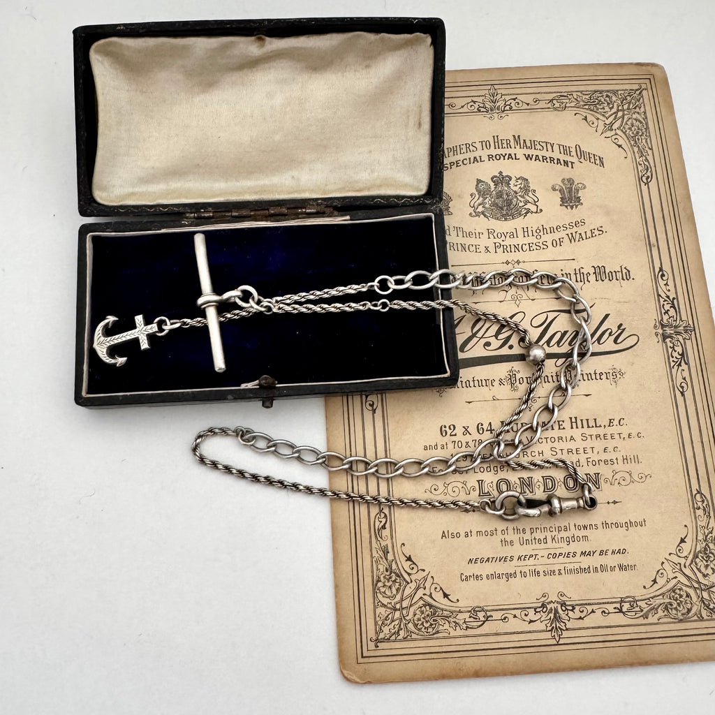 Antique silver albertina chain necklace with an anchor pendant on a vintage box and antique advertising material.