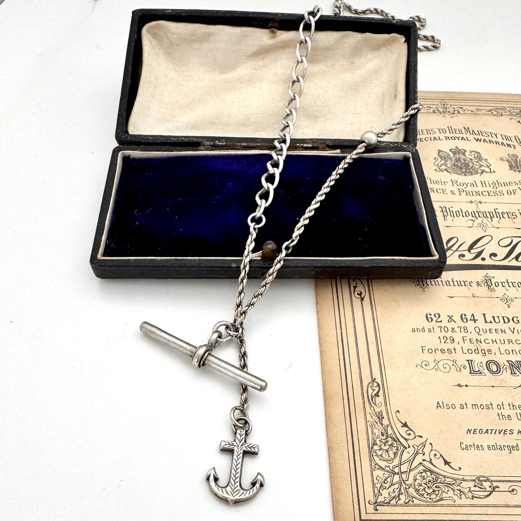Antique silver albertina chain necklace with an anchor pendant on a vintage box and antique advertising material.