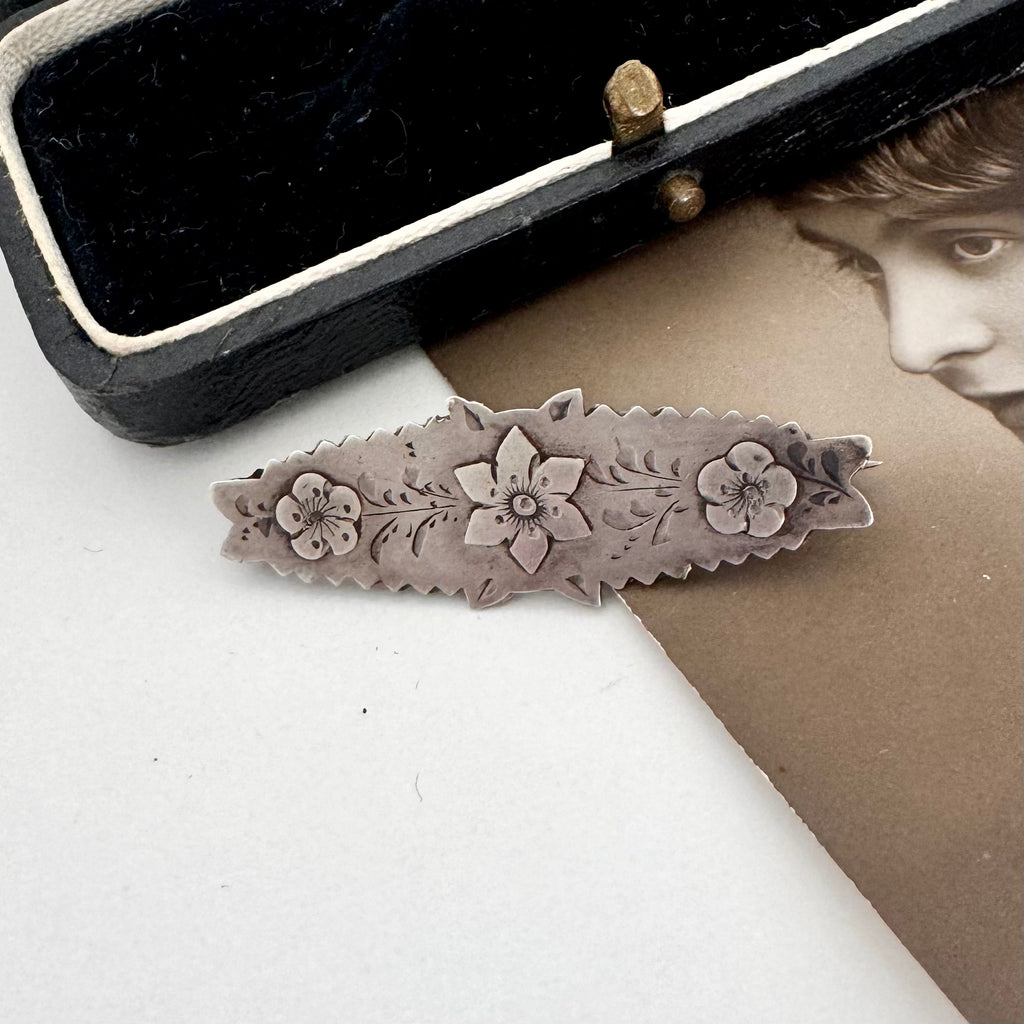 Victorian silver floral sweetheart brooch displayed inside an open black velvet jewelry box with a cream lining, with a vintage portrait card partially visible underneath.