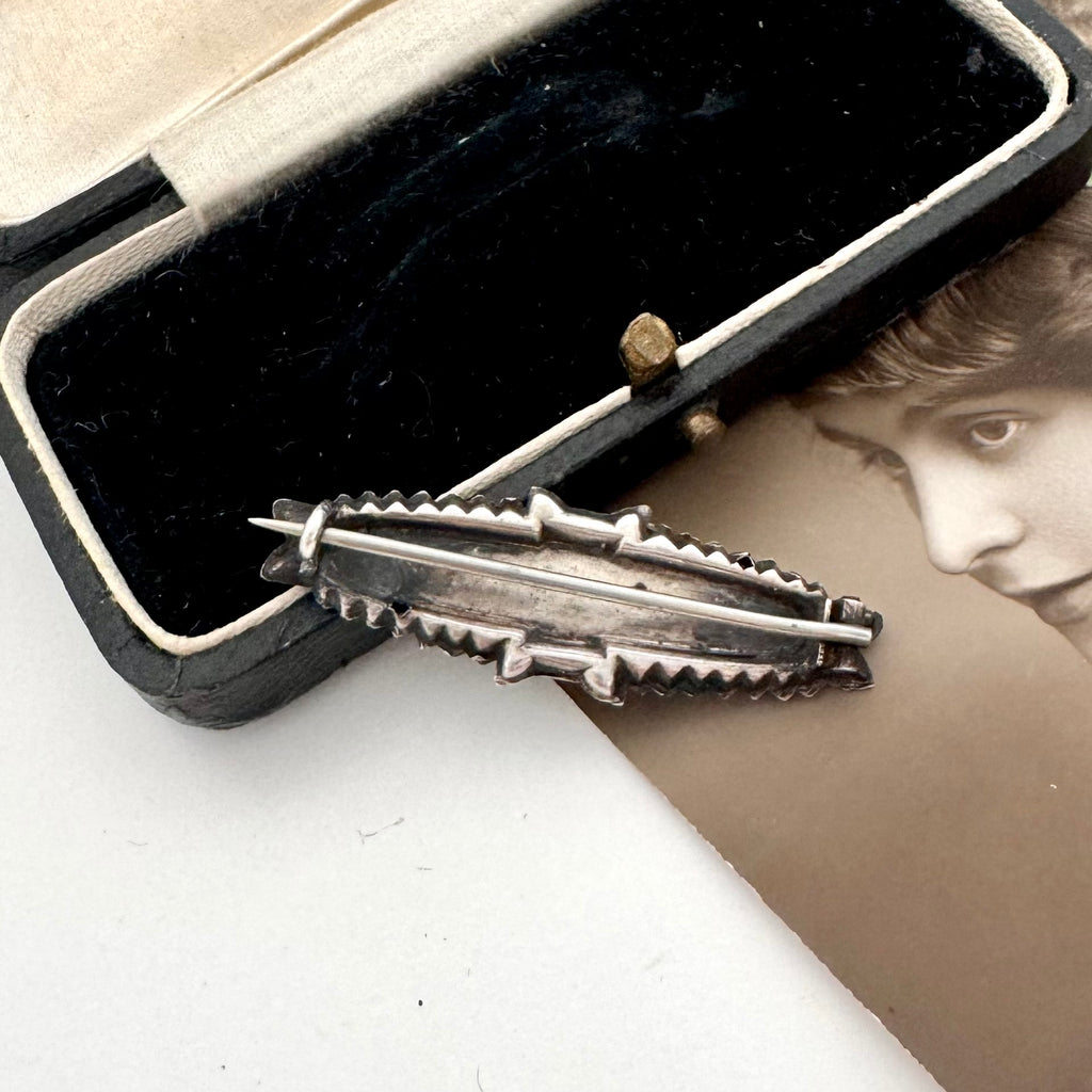 Back of Victorian silver floral sweetheart brooch displayed inside an open black velvet jewelry box with a cream lining, with a vintage portrait card partially visible underneath.