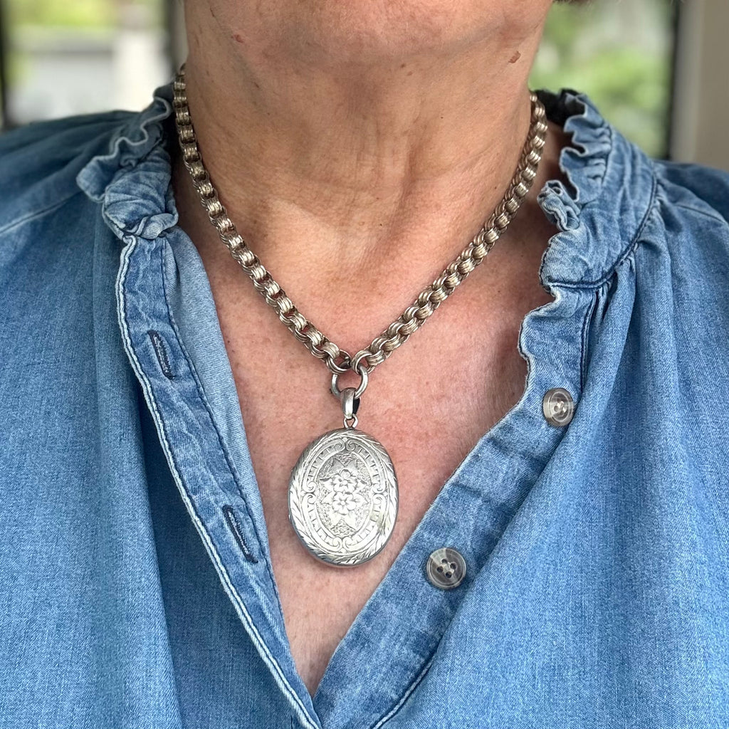 Person wearing a Victorian silver necklace with a pendant, visible under a blue denim shirt.