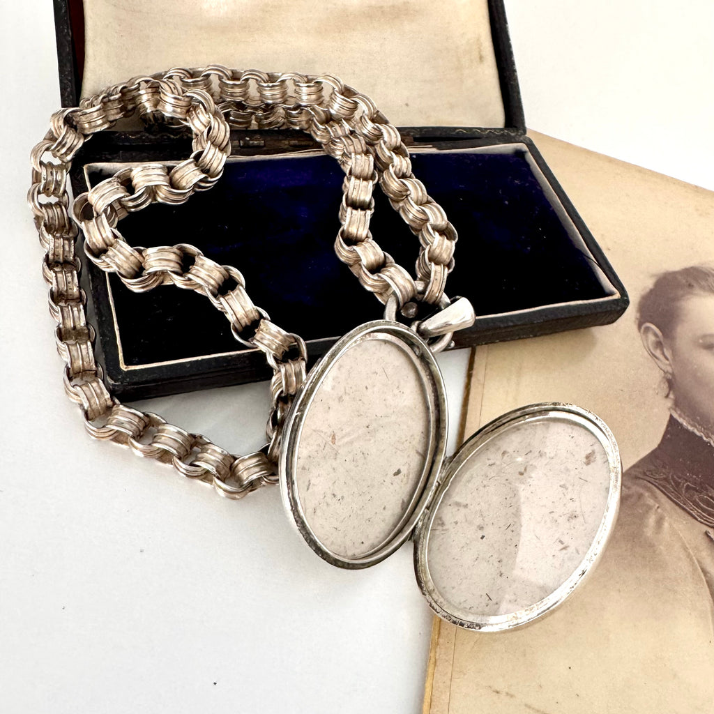 Victorian silver belcher chain with an open decorative locket on a white surface next to an old photograph.