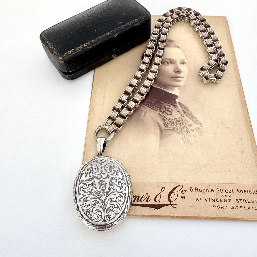 Victorian silver belcher chain with a decorative locket on a white surface next to an old photograph.