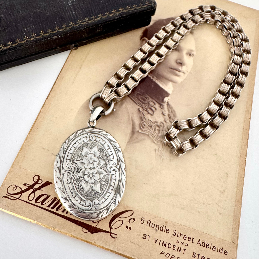 Victorian silver belcher chain with a decorative locket on a white surface next to an old photograph.
