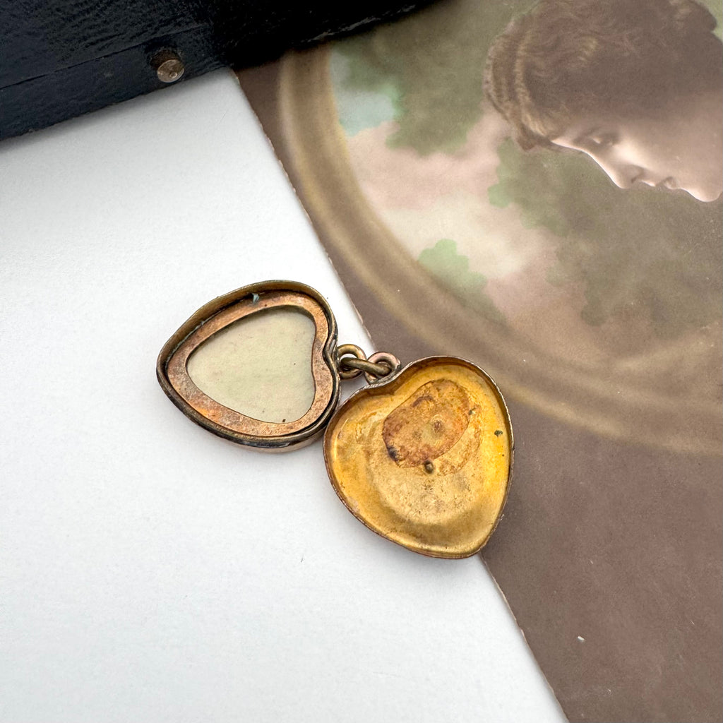 Heart-shaped gold locket with a vintage photograph in the background