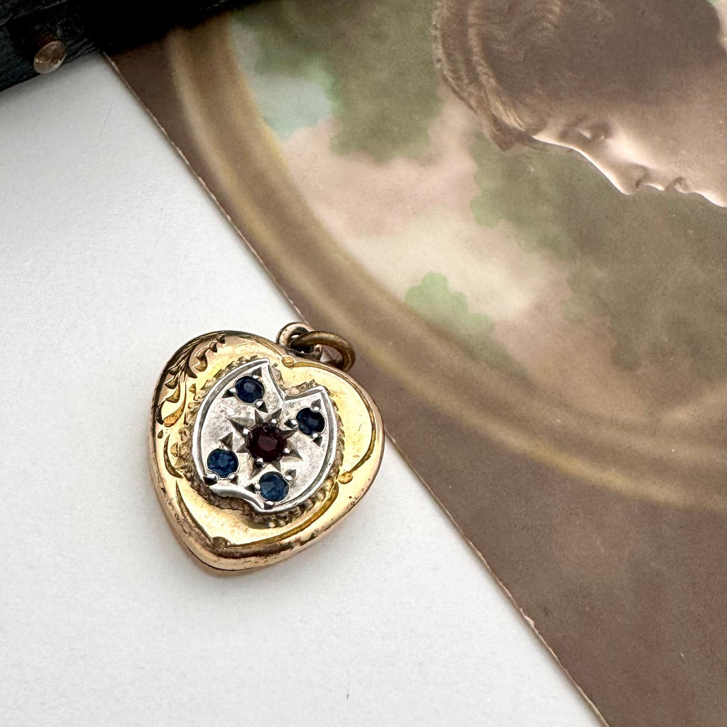 Vintage heart-shaped locket with gemstones on a white surface with an old photograph in the background.