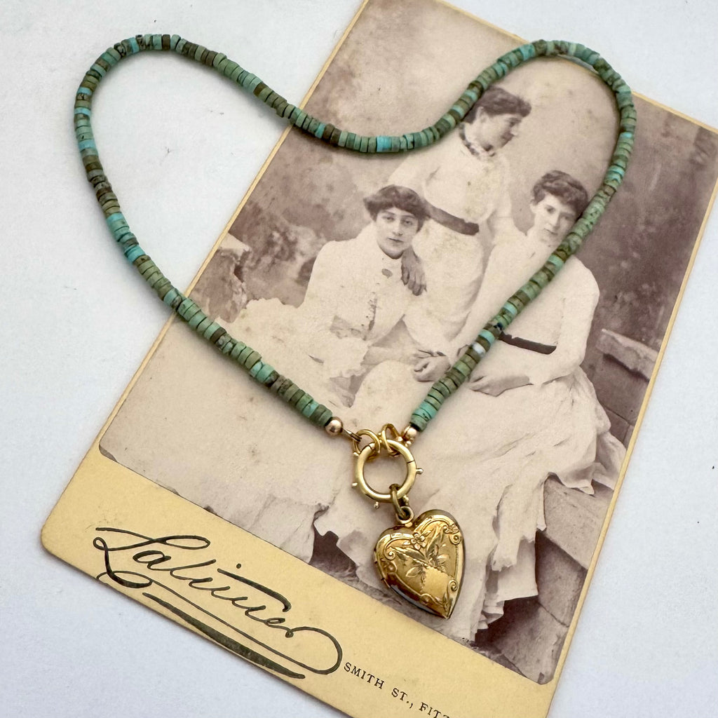 A heart-shaped turquoise bead necklace with a gold heart pendant, displayed on top of a vintage photograph card.