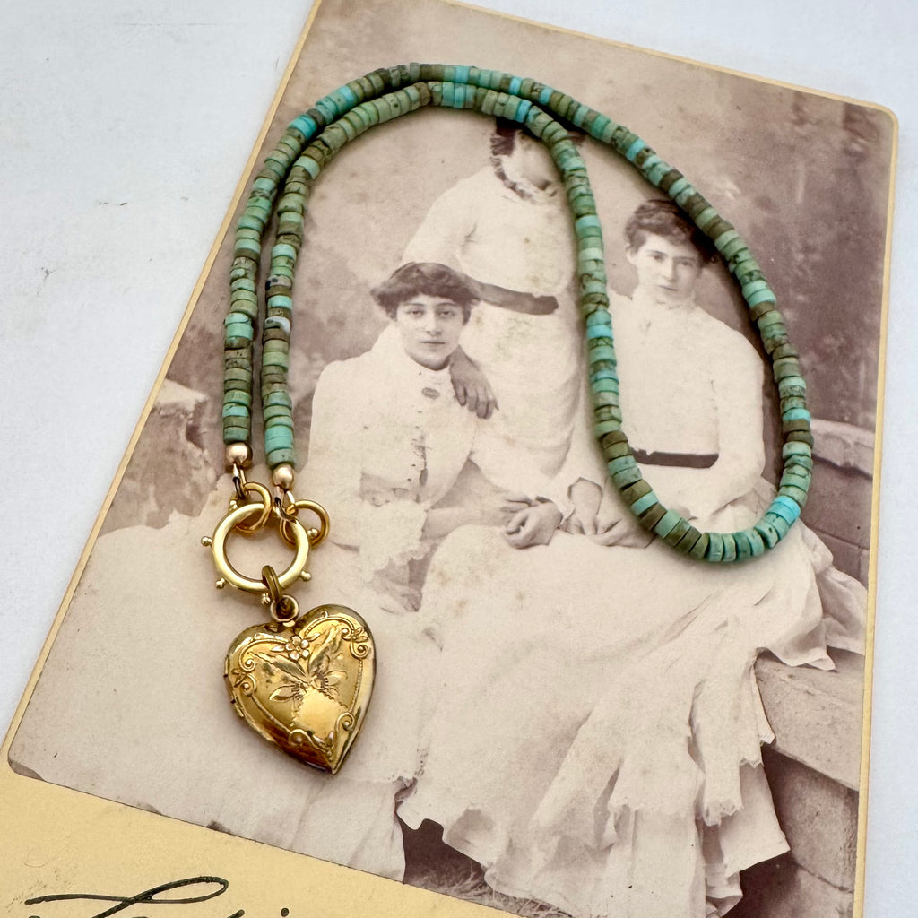 A vintage Carl Art gold heart-shaped locket pendant and a beaded turquoise-blue chain, displayed on a vintage printed card.