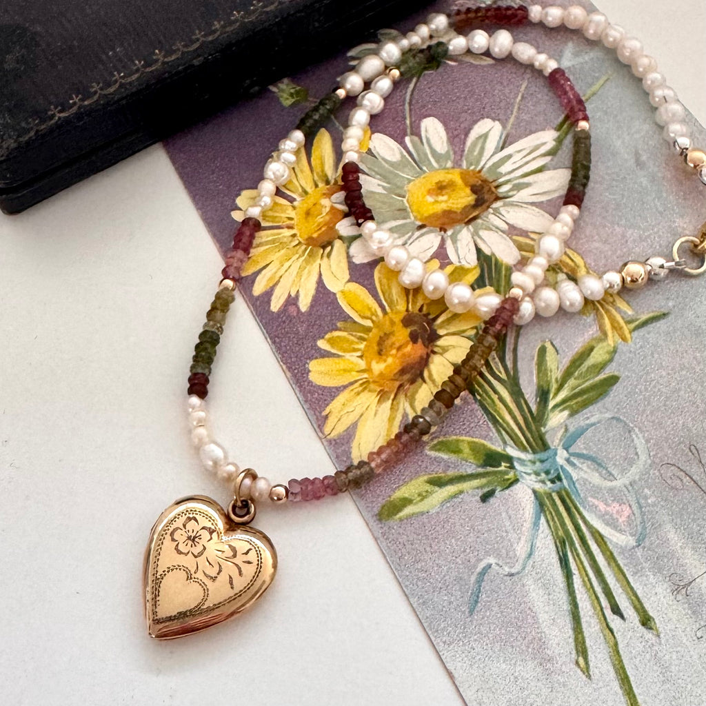 Vintage rolled gold Varga heart locket and tourmaline and pearls necklace on a vintage postcard and with an old jewellery box