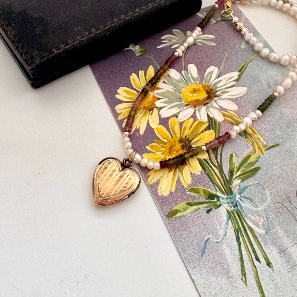 Vintage rolled gold Varga heart locket and tourmaline and pearls necklace on a vintage postcard and with an old jewellery box