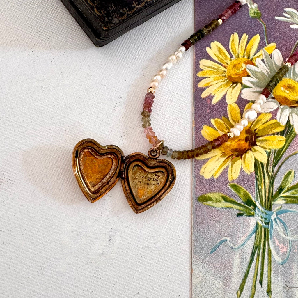 Necklace with a vintage Vargas heart locket on a surface with flowers and a book in the background