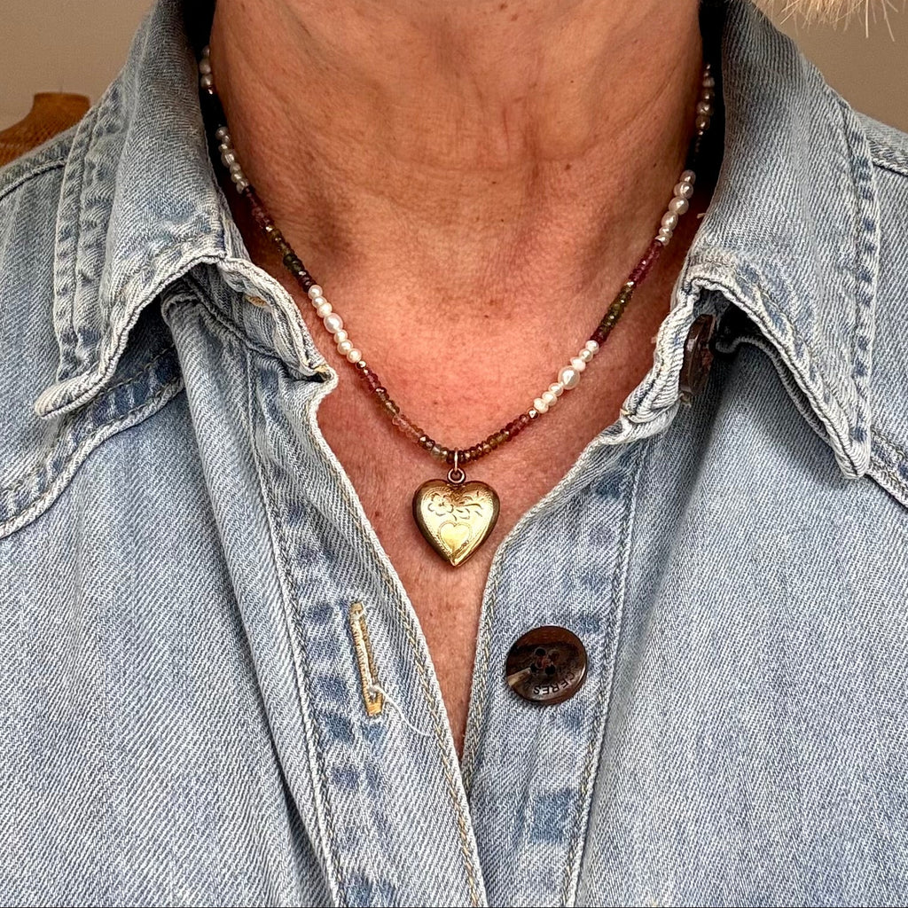 Person wearing a denim shirt with a necklace featuring a heart-shaped pendant.