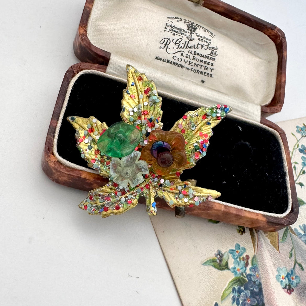 A vintage European hand wired gold-toned brooch shaped like a lotus flower with green, amber, and multicolor rhinestone accents, displayed inside an open wooden jewelry box with cream lining.