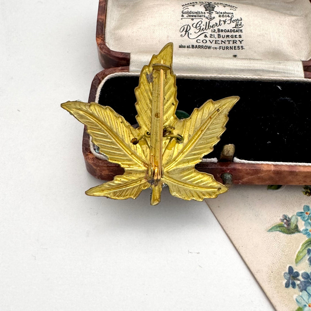 Back of vintage European hand wired gold-toned brooch shaped like a lotus flower with green, amber, and multicolor rhinestone accents, displayed inside an open wooden jewelry box with cream lining.