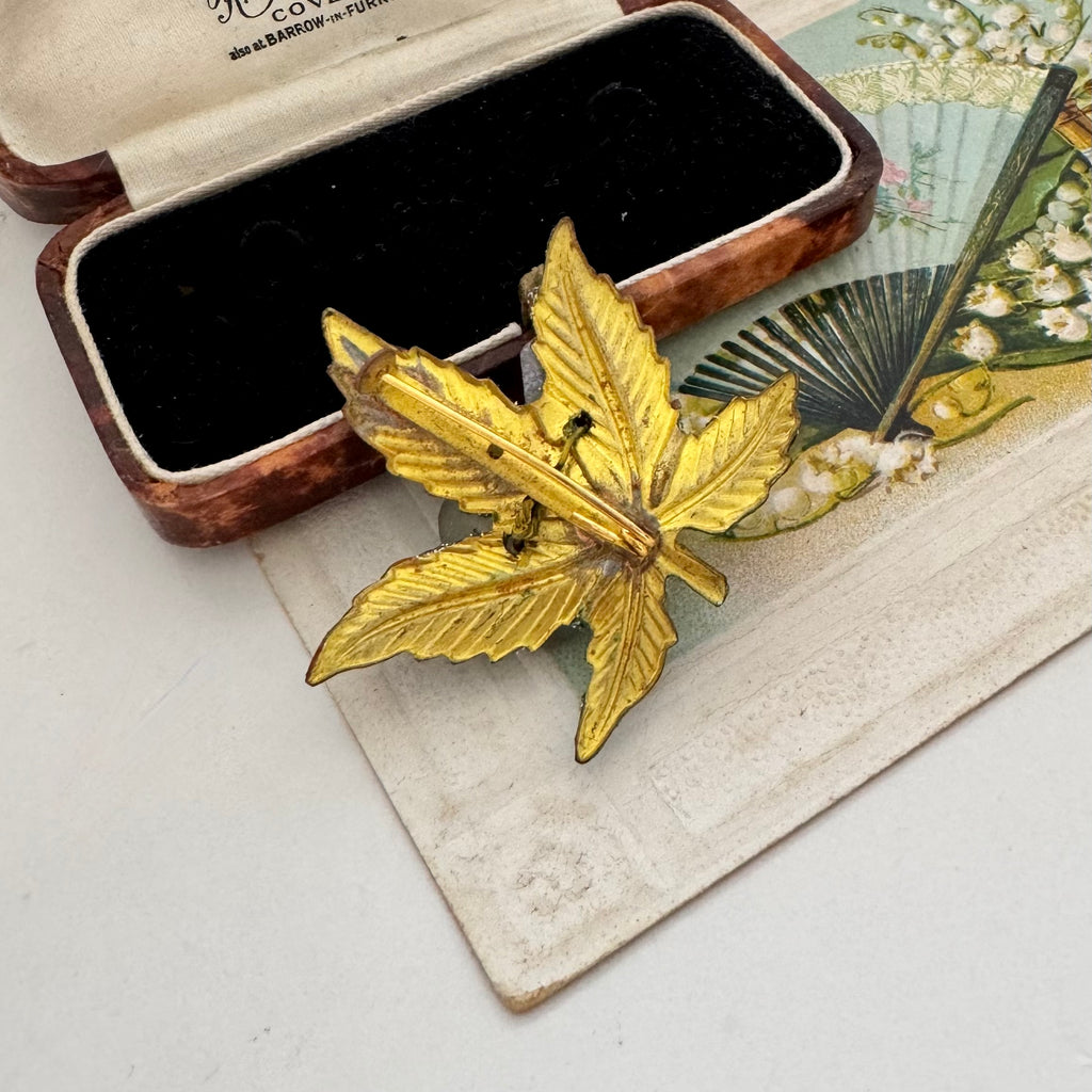 Back of vintage European floral brooch displayed next to an open vintage wooden jewelry box on a beige textured paper surface.