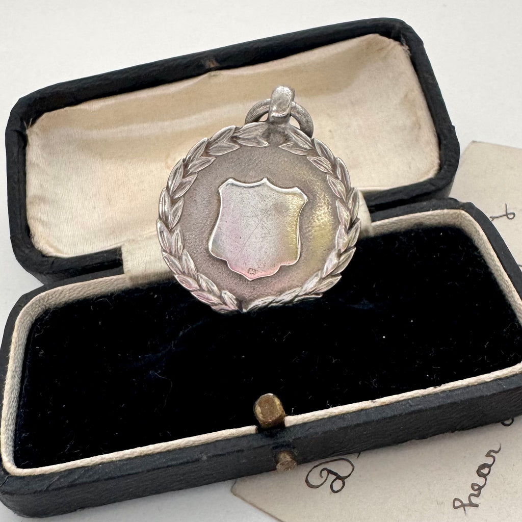 Silver medallion with a shield design in an open black velvet box.