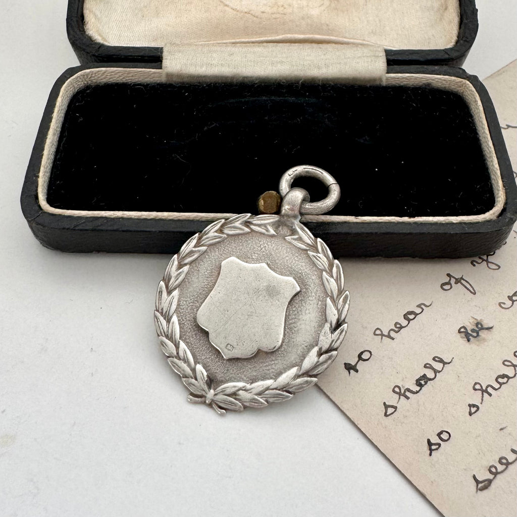 Silver medal with wreath design in an open box on a white surface