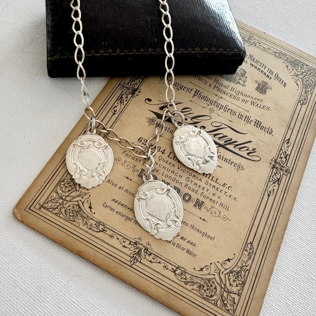 Silver necklace with three vintage watch fob pendants on an old document background