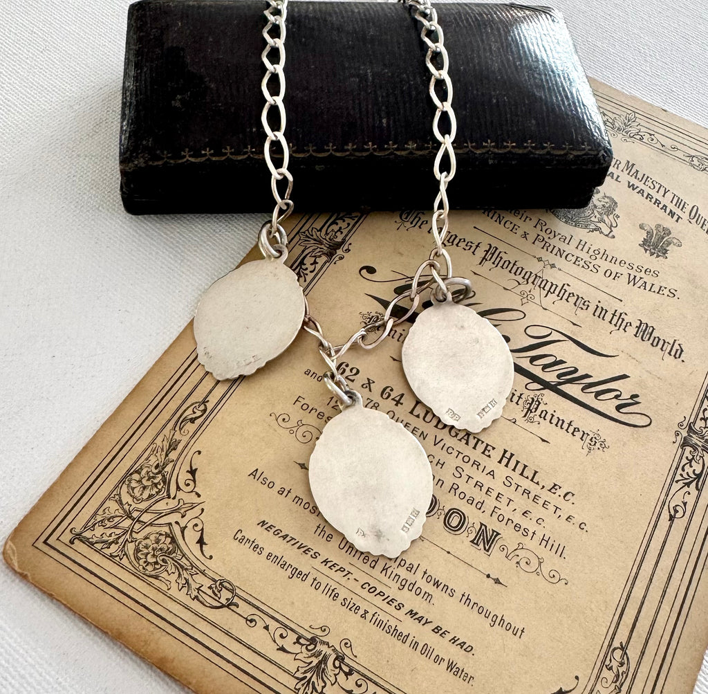 Silver necklace with three vintage watch fob pendants on an old document background