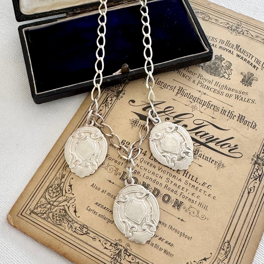 Silver necklace with three vintage watch fob pendants on an old document background
