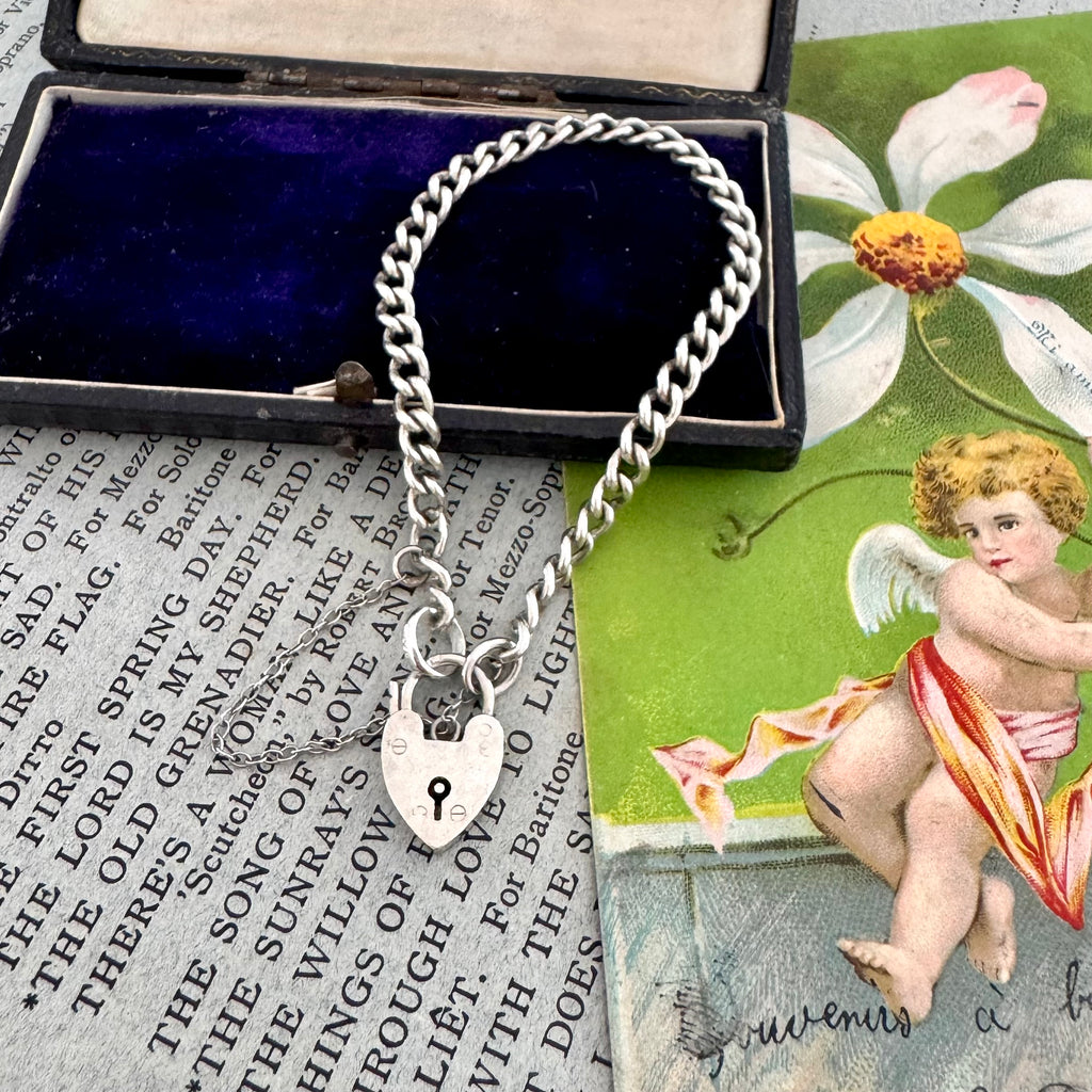 Silver chain bracelet with a lock charm on an old book page with an angel illustration.