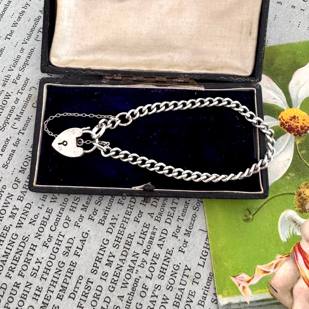 Silver bracelet with heart charm in an open jewelry box on a vintage-style magazine background.
