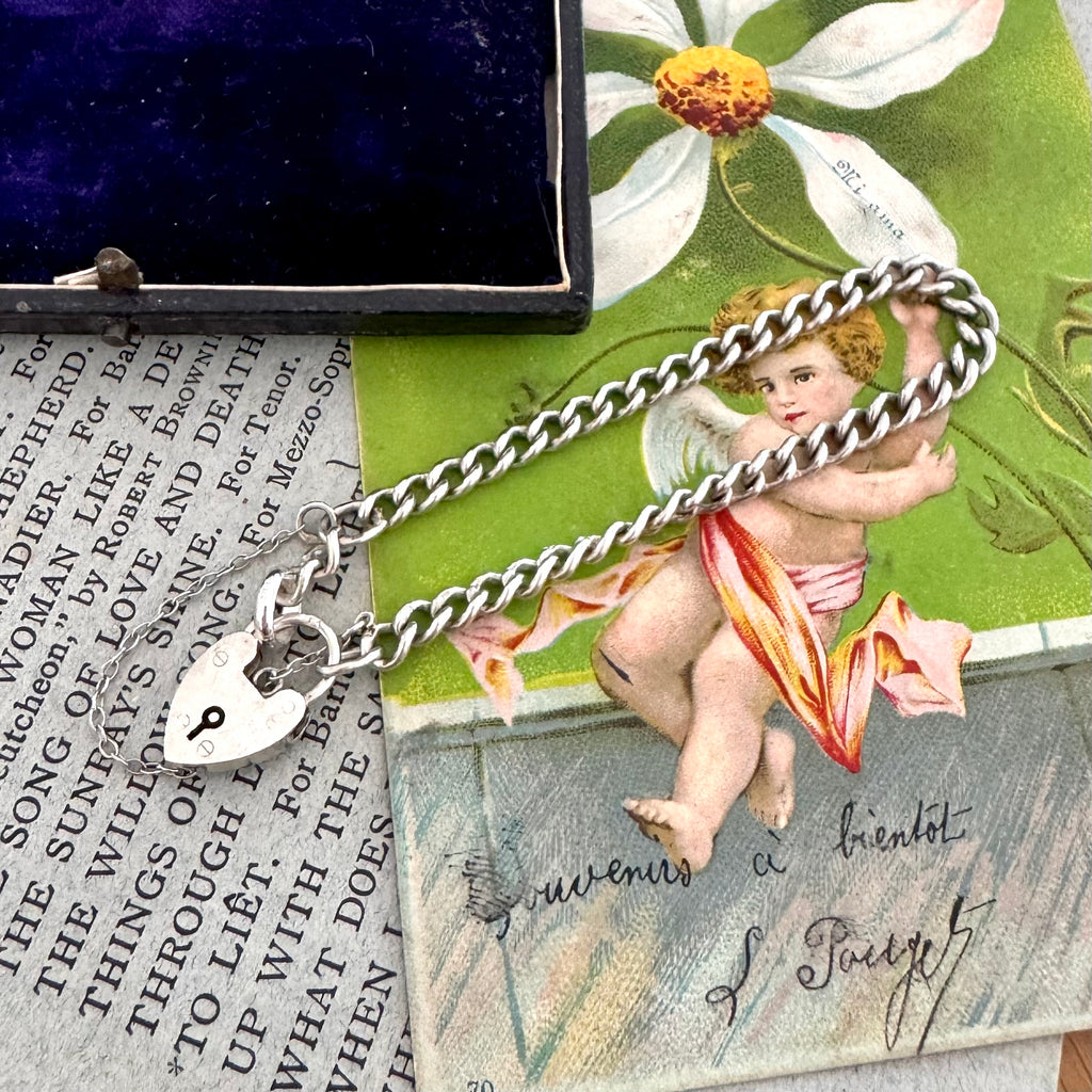 Silver chain bracelet with a heart charm on a vintage-style card with text and floral design.