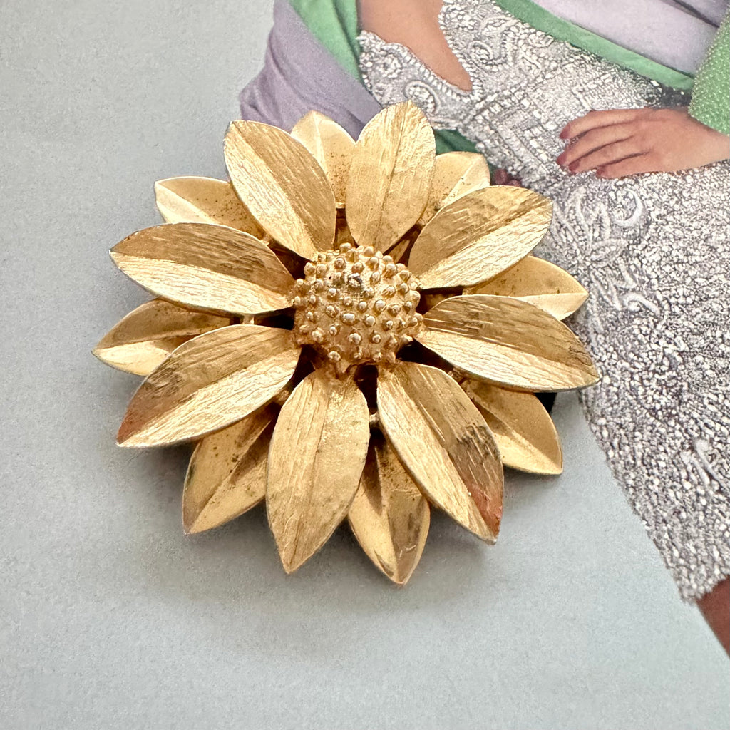 Vintage 1964 Sarah Coventry "Satin Petals" sunflower brooch with rare Canada mark on the cover of a Vogue book