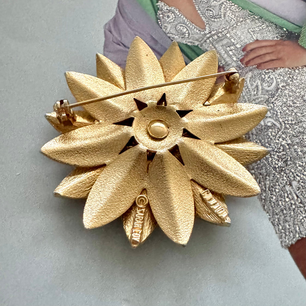 Vintage 1964 Sarah Coventry "Satin Petals" sunflower brooch with rare Canada mark on the cover of a Vogue book