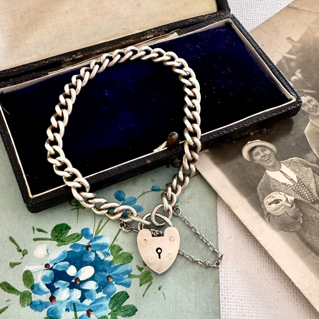 Silver chain bracelet with a heart-shaped lock charm on a floral and vintage-style background