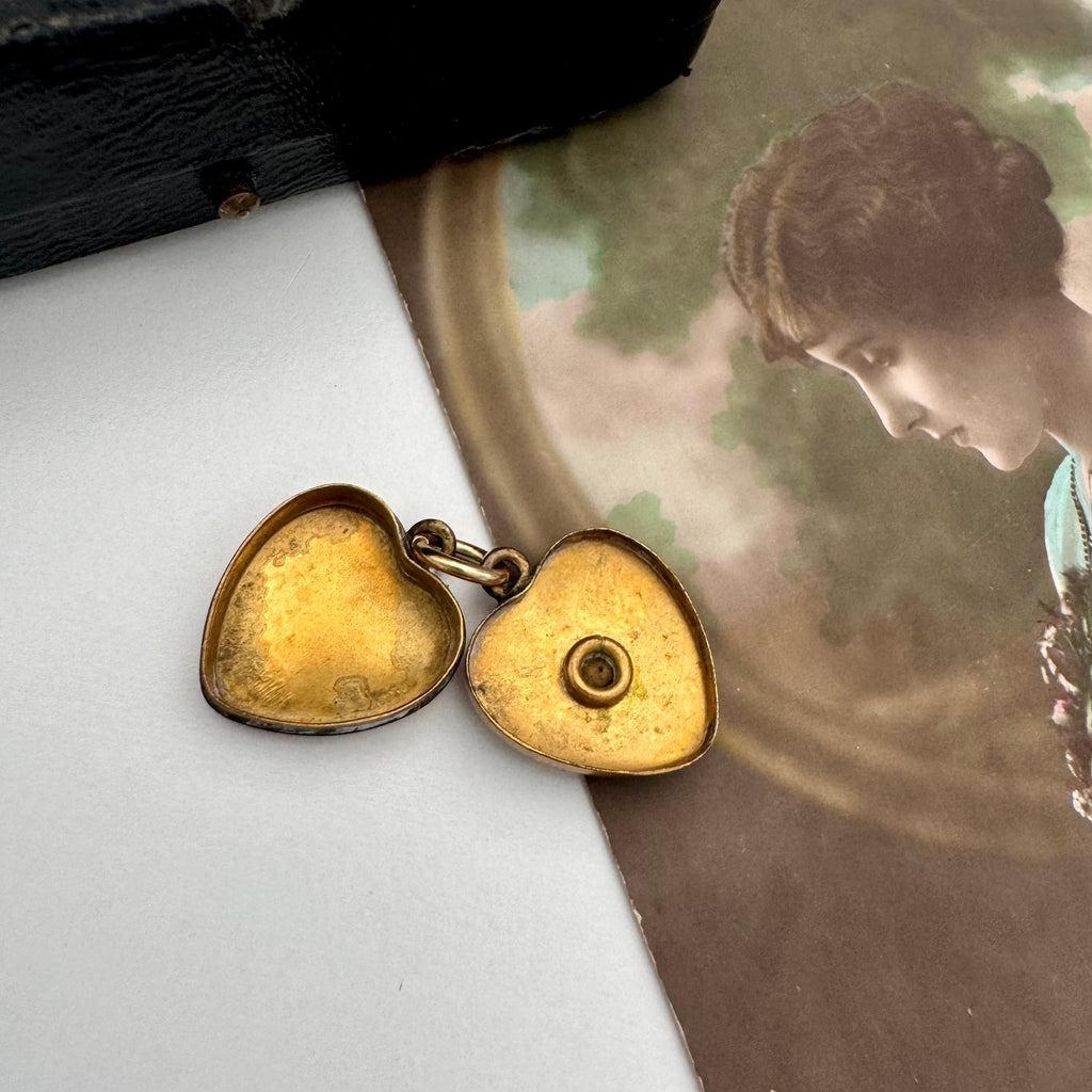 Heart-shaped gold locket on a white surface with an antique-style portrait in the background.
