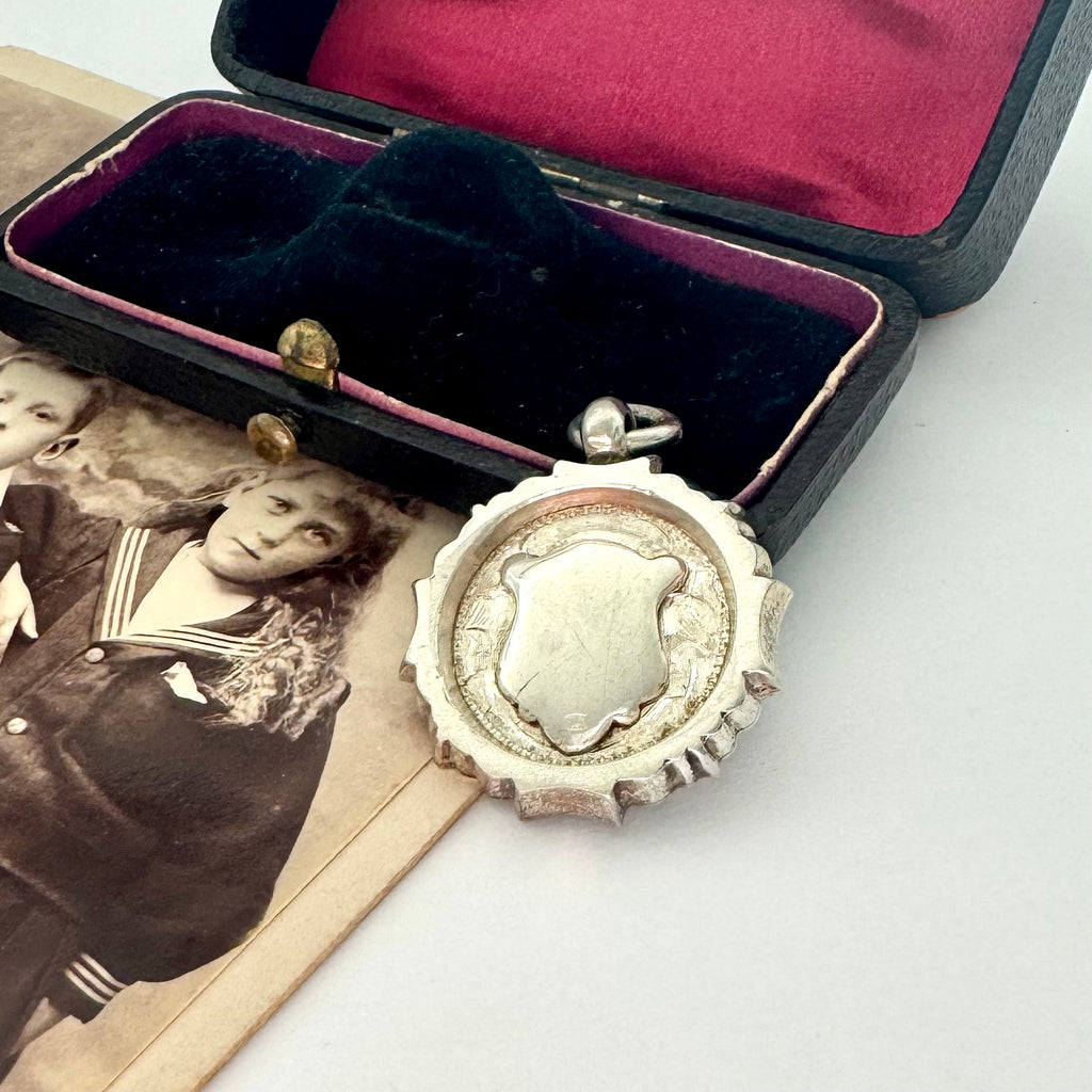 Vintage 1937 Chester silver watch fob on a white surface next to an open box with velvet interior.