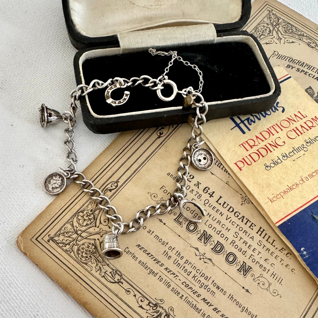 Silver charm bracelet made from vintage Harrods christmas pudding charms in an open jewelry box on top of an old advertisement for Harrods.