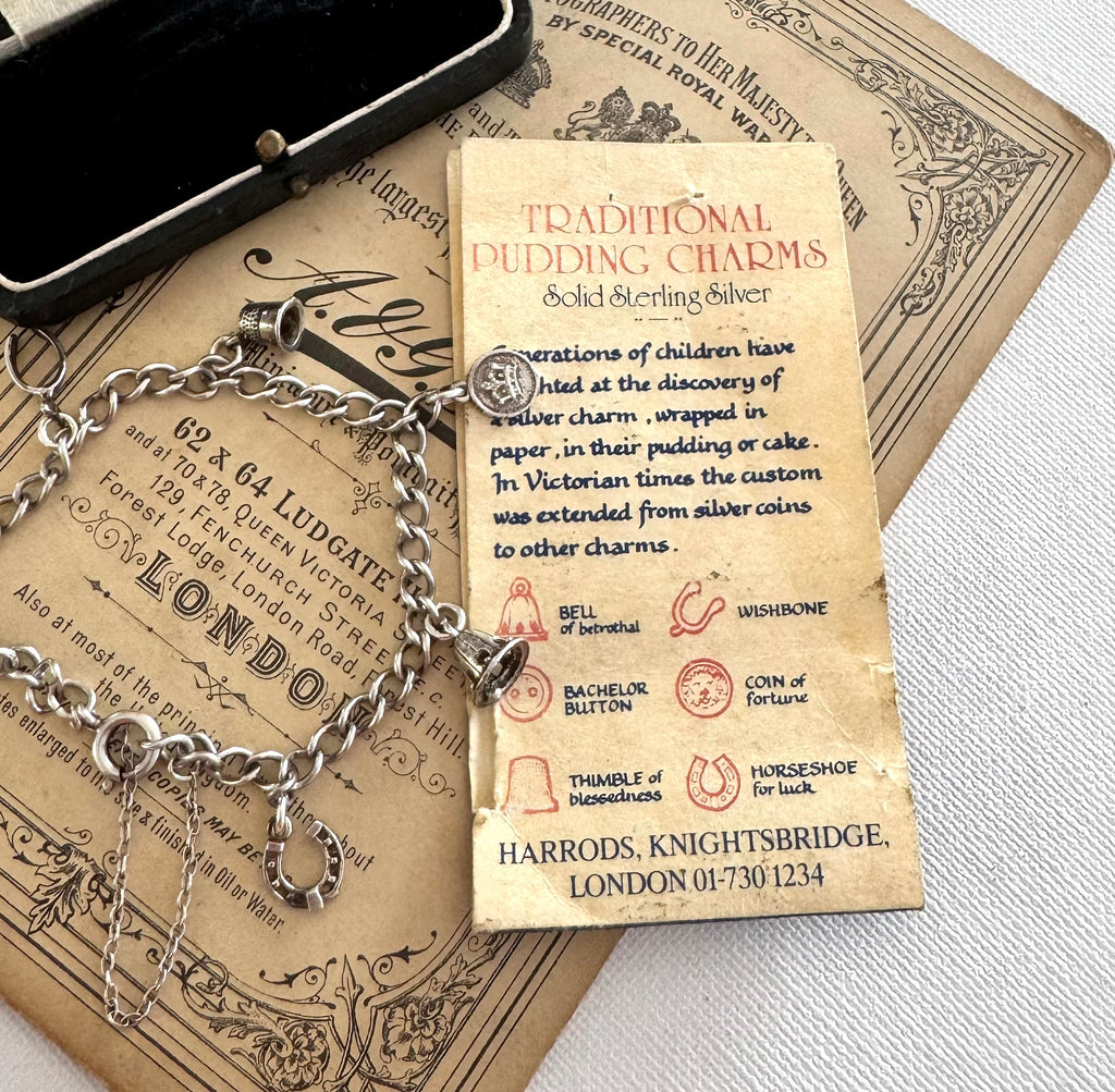 Silver charm bracelet made from vintage Harrods christmas pudding charms in an open jewelry box on top of an old advertisement for Harrods.