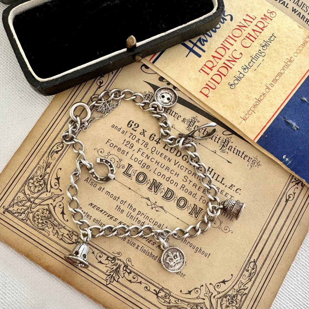Silver charm bracelet made from vintage Harrods christmas pudding charms in an open jewelry box on top of an old advertisement for Harrods.