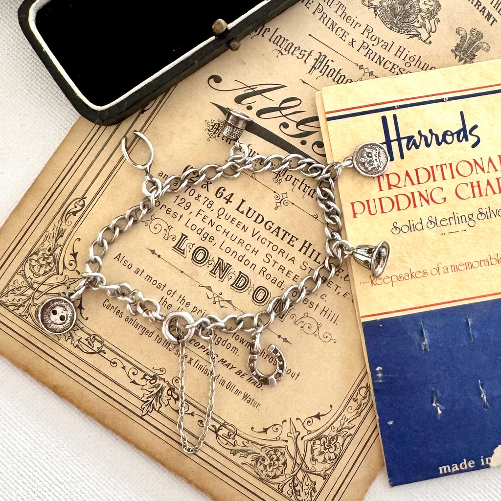 Silver charm bracelet made from vintage Harrods christmas pudding charms in an open jewelry box on top of an old advertisement for Harrods.