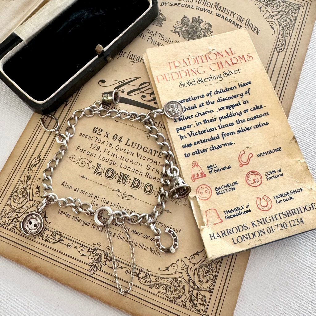 Silver charm bracelet made from vintage Harrods christmas pudding charms in an open jewelry box on top of an old advertisement for Harrods.