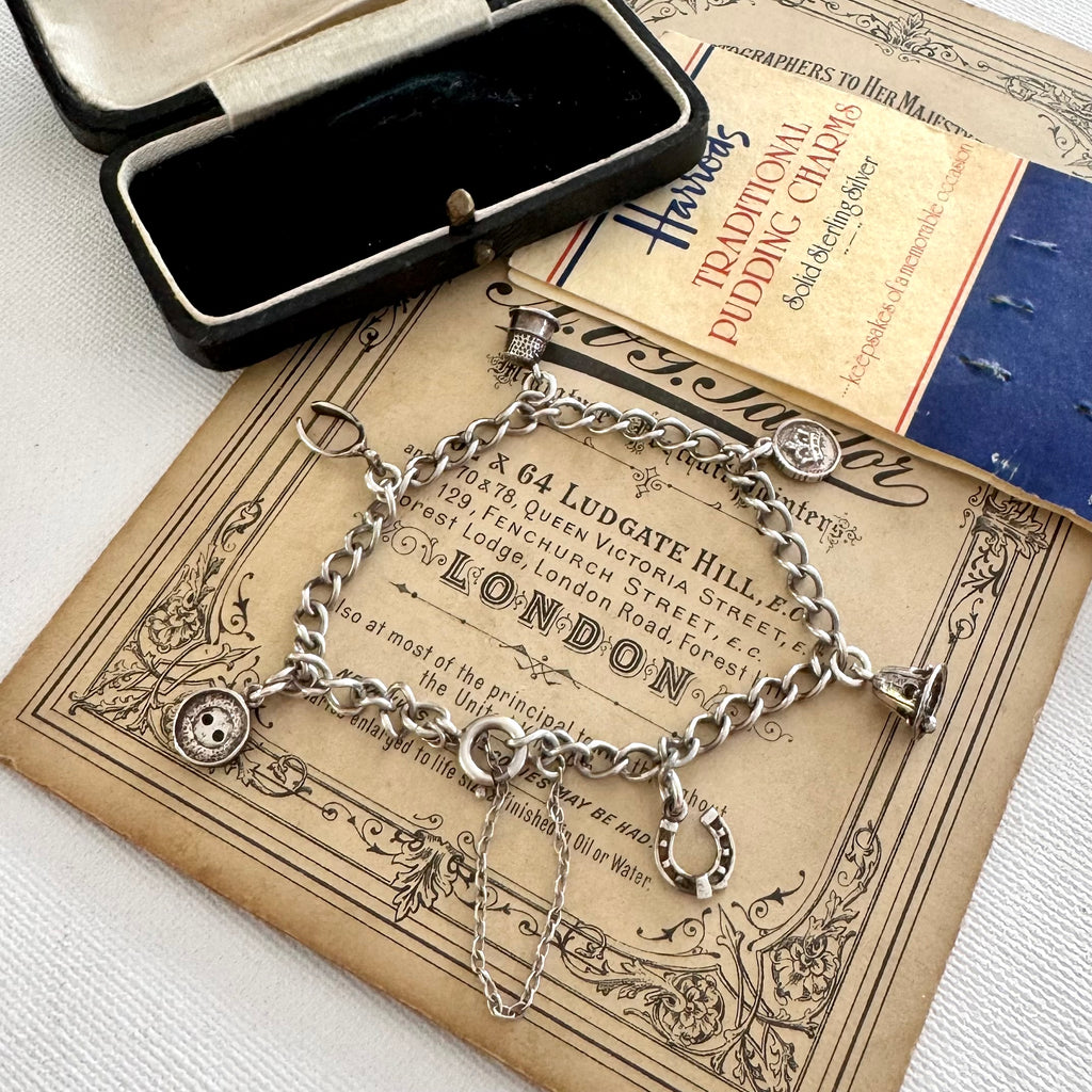 Silver charm bracelet made from vintage Harrods christmas pudding charms in an open jewelry box on top of an old advertisement for Harrods.