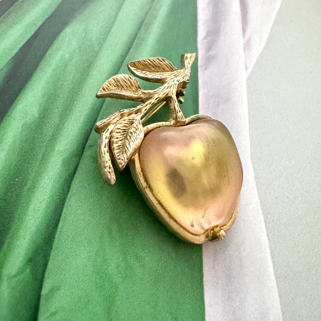 Rare GB stamped Sarah Coventry gold apple-shaped brooch with leaves on a green and white fabric background