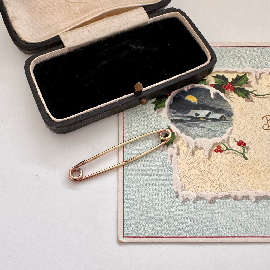 Gold safety pin on a textured surface with a decorative card in the background