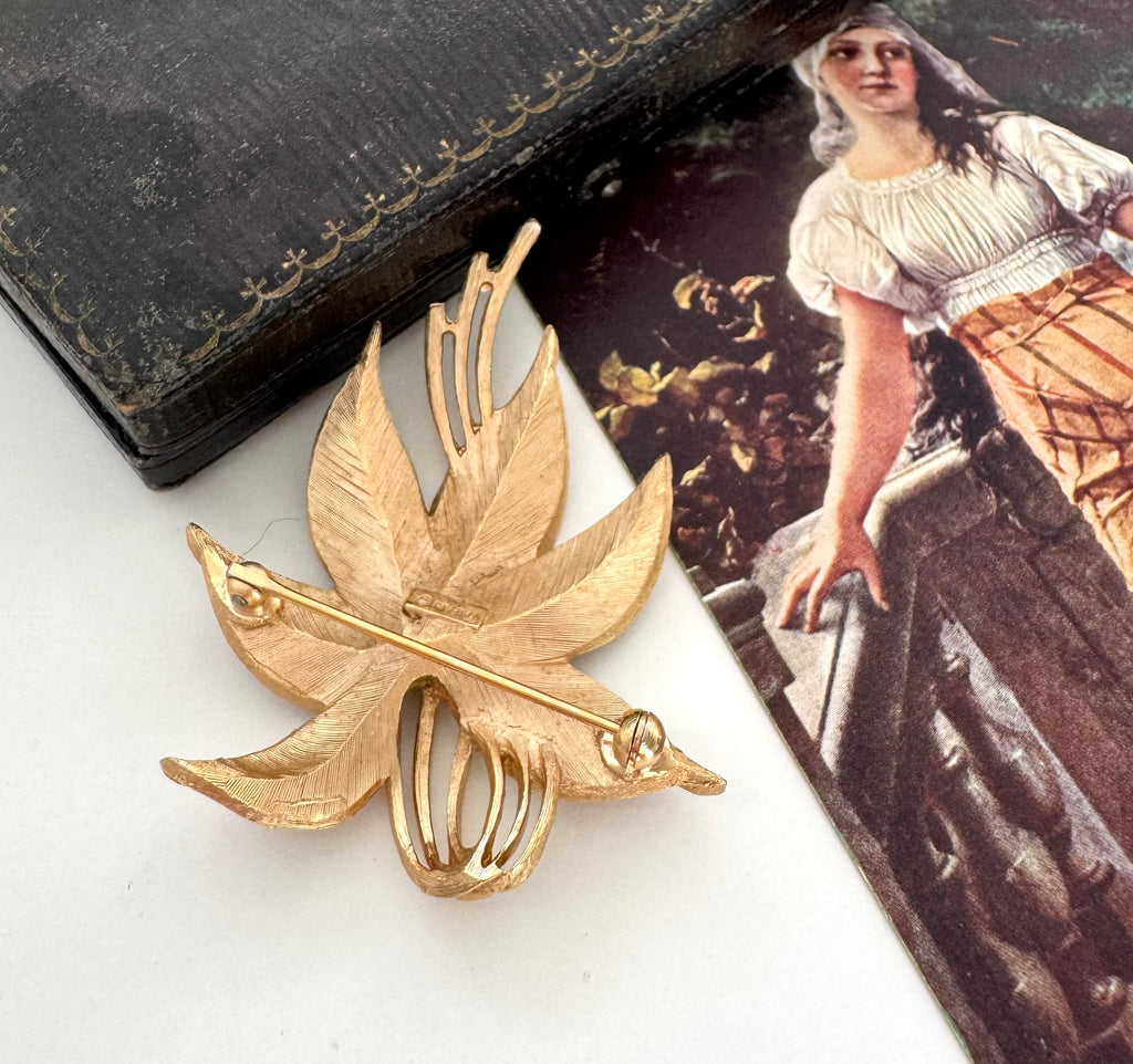 Vintage Crown Trifari leaf-shaped brooch on a white surface with a vintage-style magazine in the background.